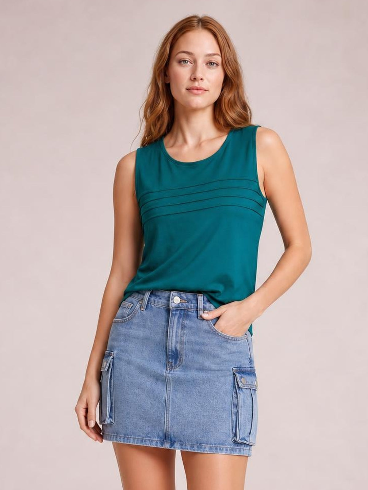 A model poses in a light blue cargo denim skirt with a high waist, button fly, belt loops, straight mini silhouette, and roomy flap pockets, one hand tucked in.
