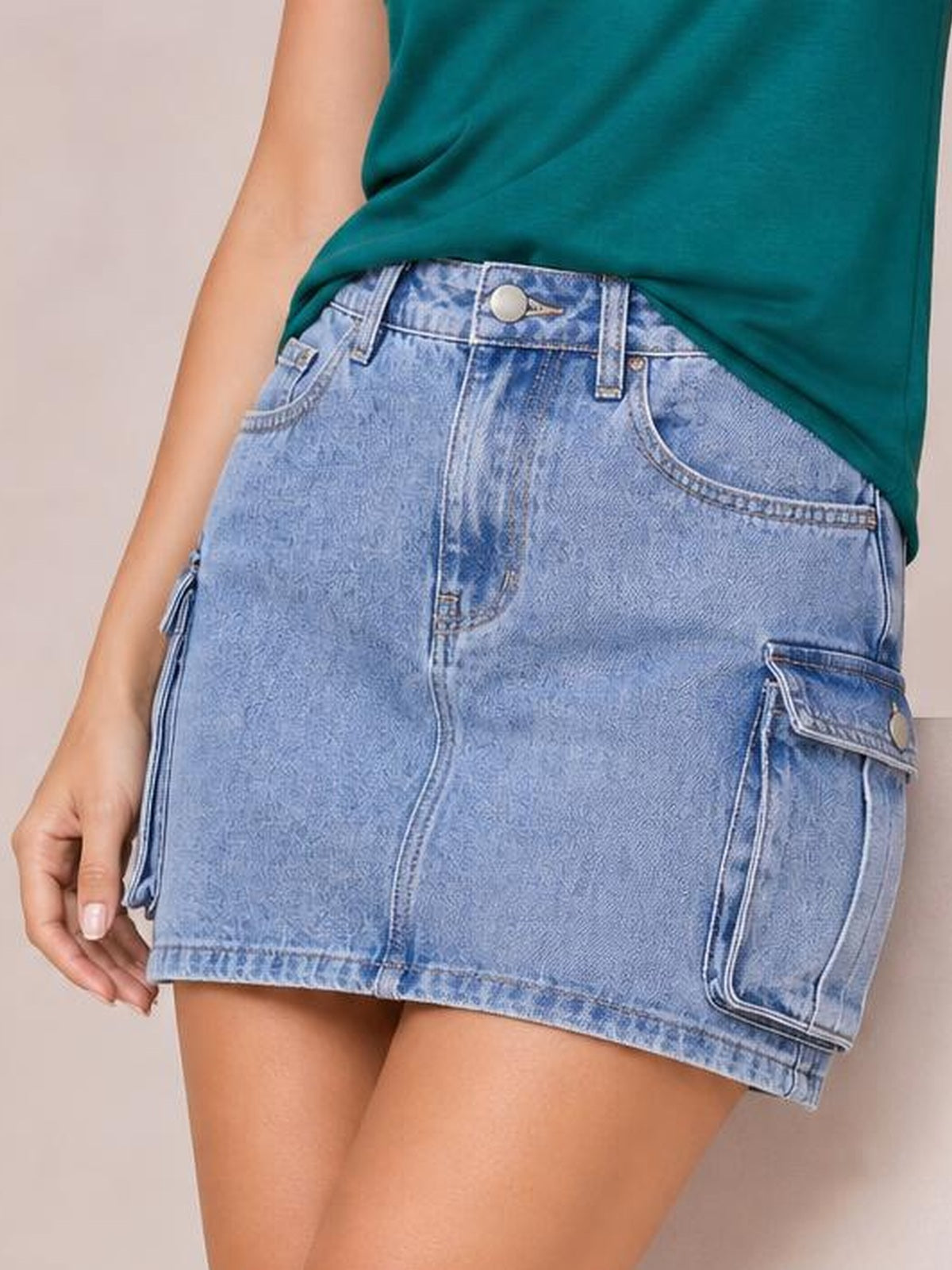 Model poses in a light blue denim cargo skirt with a structured mini silhouette, belt loops, front pockets, stitched seams, and a flap cargo pocket.