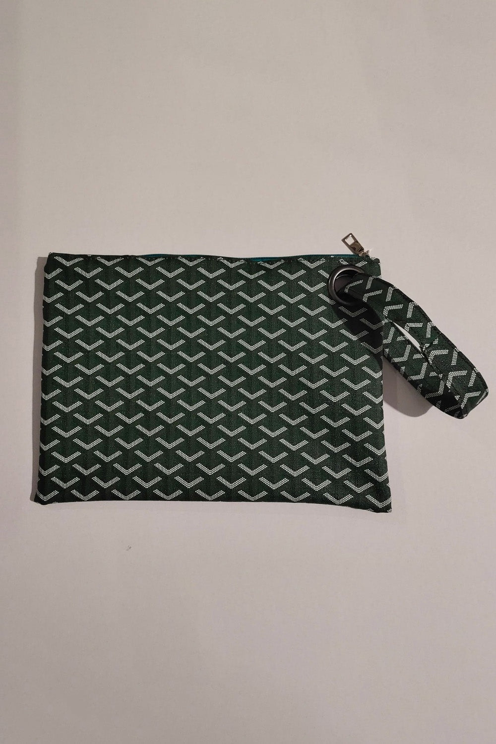 A medium rectangular dark green and white patterned PU leather wristlet features a zippered top, streamlined construction, and matching wrist strap.