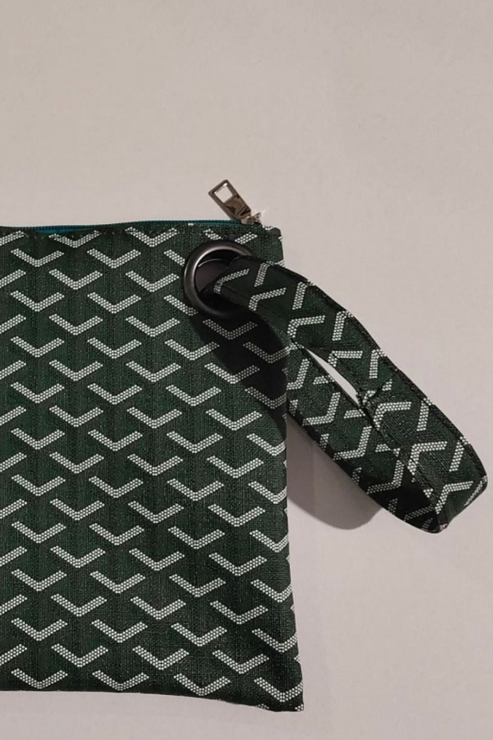 Flat-lay medium PU leather wristlet in dark green with a white geometric pattern, rectangular silhouette, top zipper, and matching wrist strap.