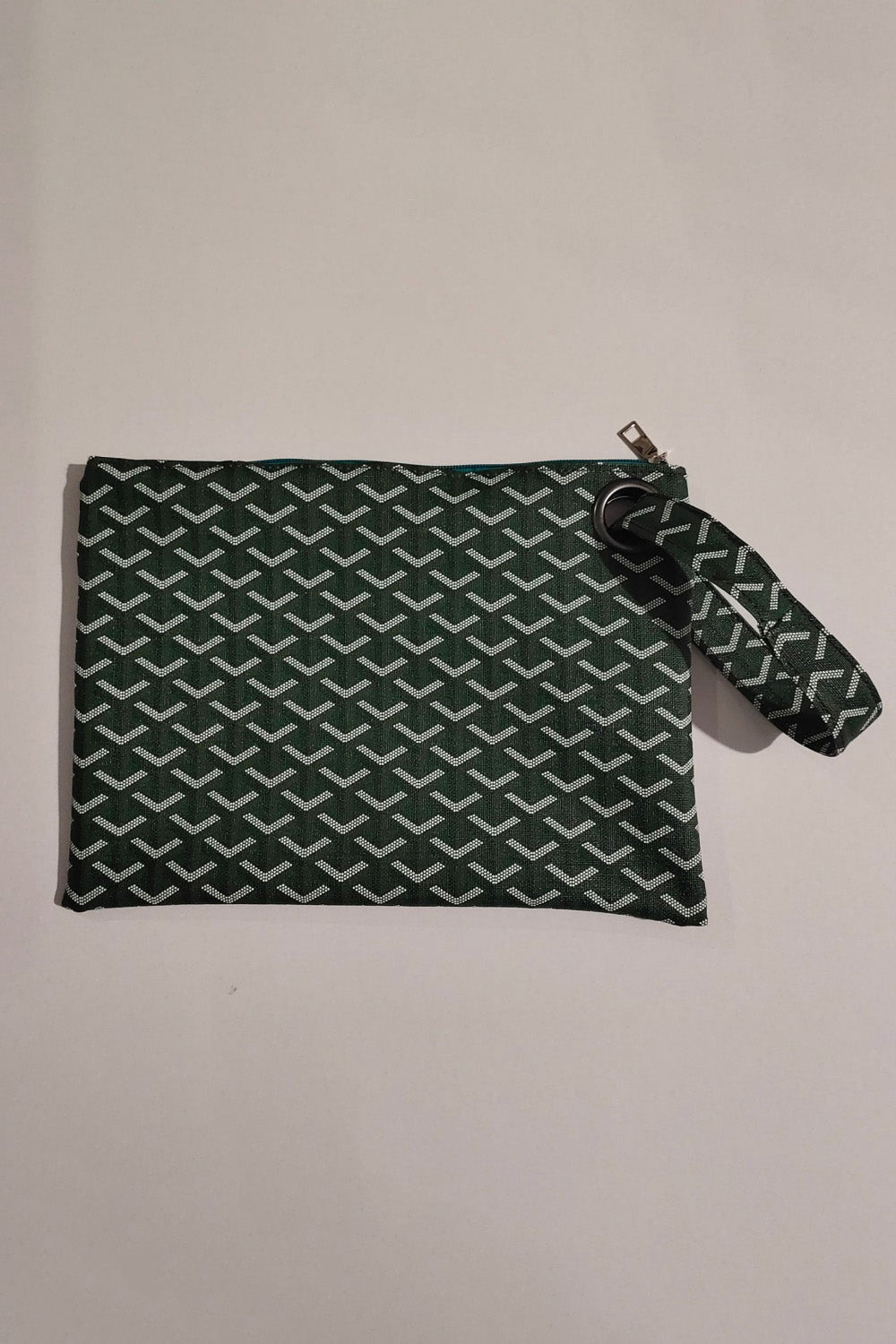 A medium rectangular dark green and white patterned PU leather wristlet features a zippered top, streamlined construction, and matching wrist strap.