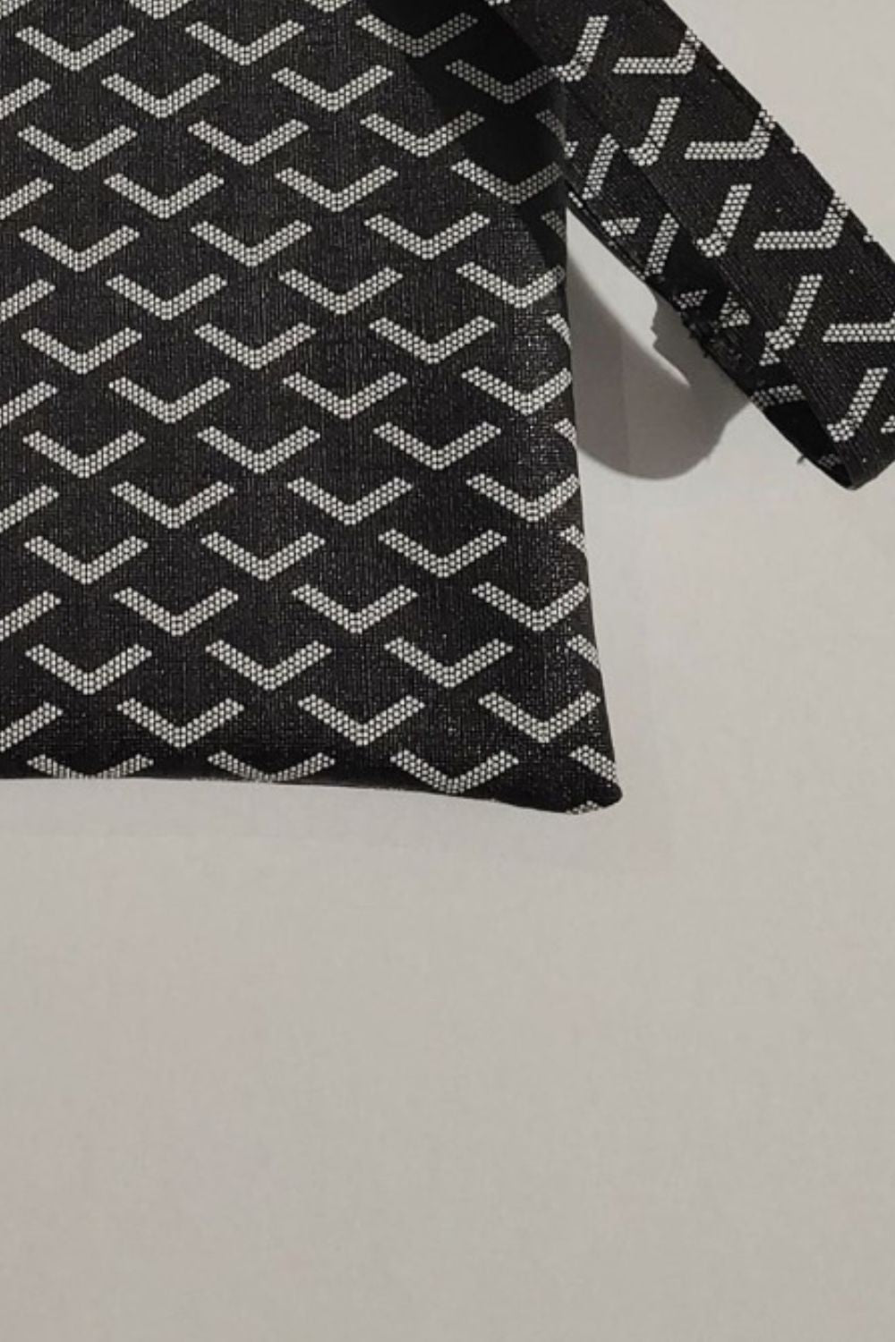 Close-up of black fabric with repeating white chevron-like motifs, showing a long sleeve and angled hem.