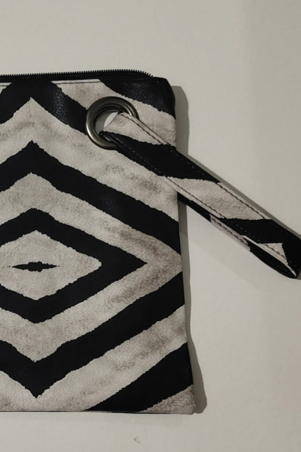 Black and cream geometric-print PU leather wristlet with a clean rectangular silhouette, zip-top construction, and a slim strap attached by a metal ring.