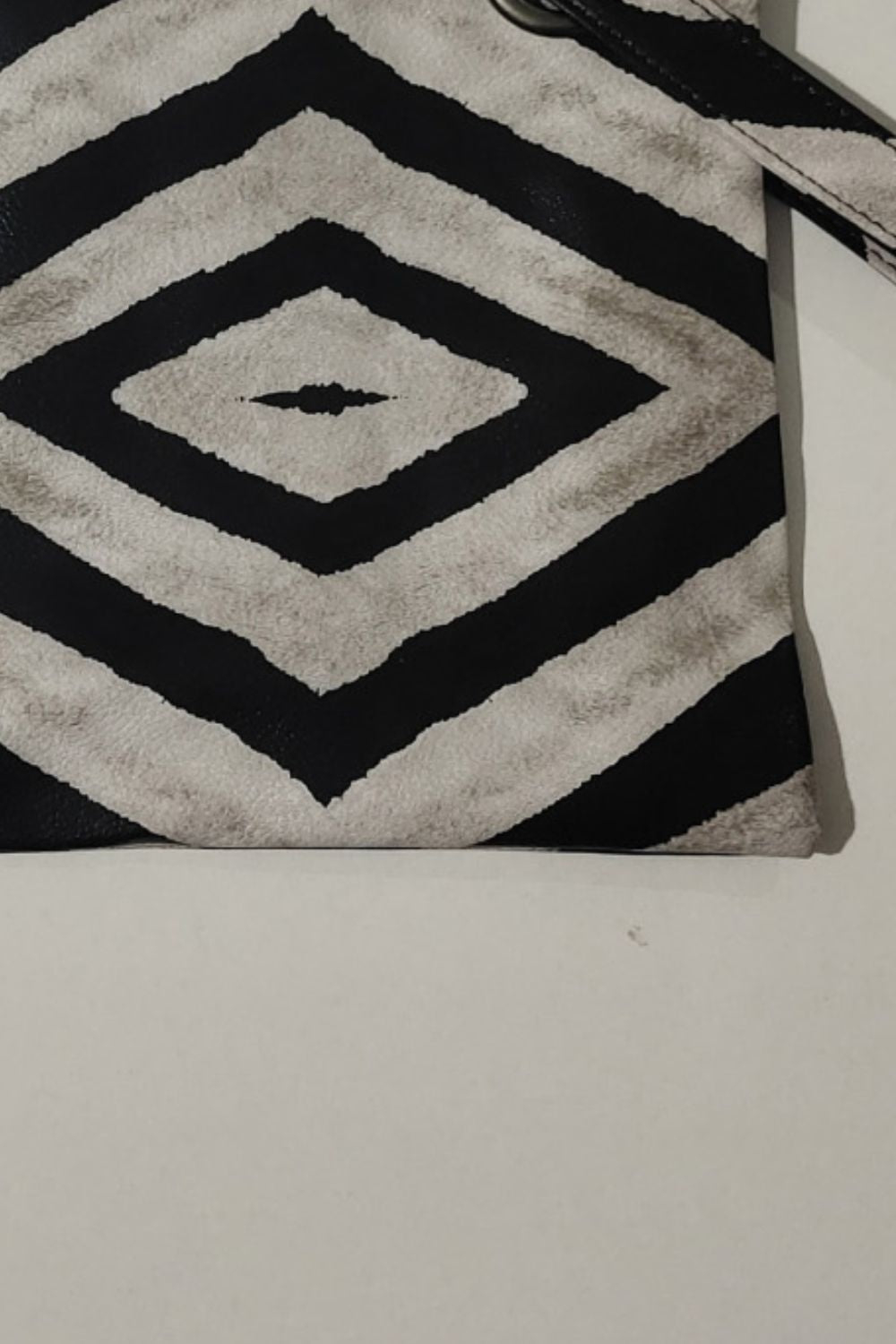 Flat-lay medium wristlet in black and cream geometric pattern, featuring a clean rectangular silhouette and polished PU leather construction.