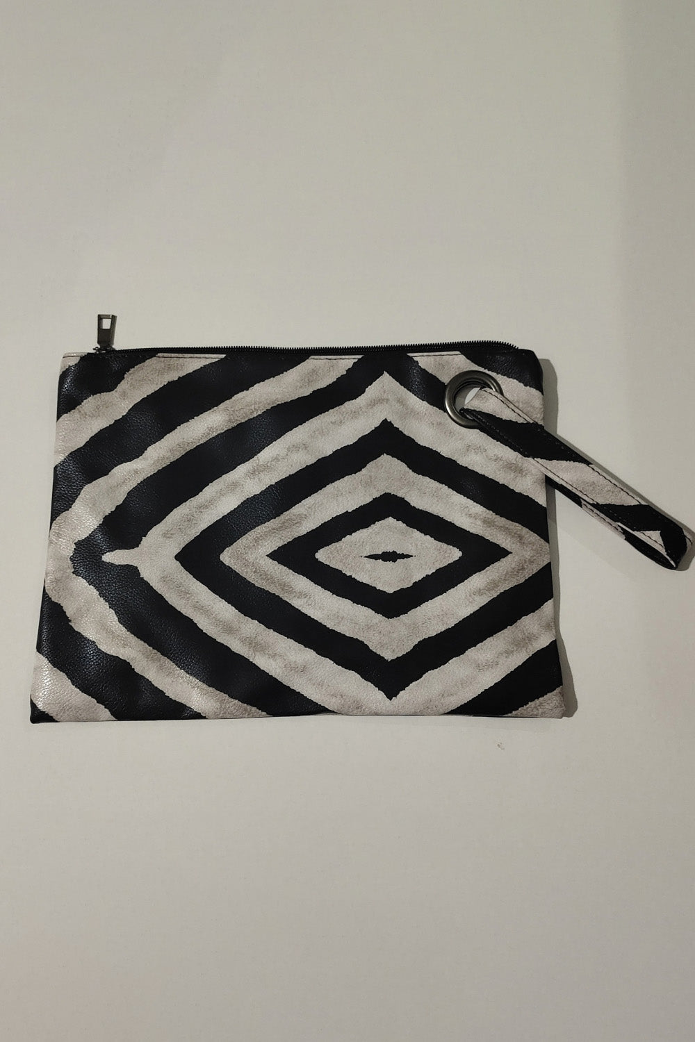 A medium rectangular PU leather wristlet features a bold black-and-cream geometric pattern, zip-top closure, and detachable wrist strap.