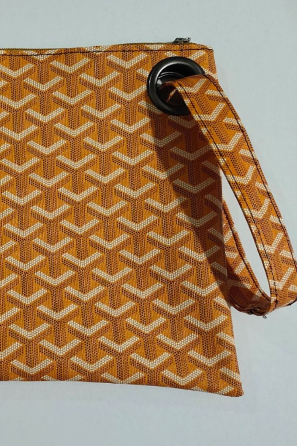 Flat-lay view of a medium orange and tan PU leather wristlet with a rectangular silhouette, zip-top closure, geometric pattern, and detachable wrist strap.