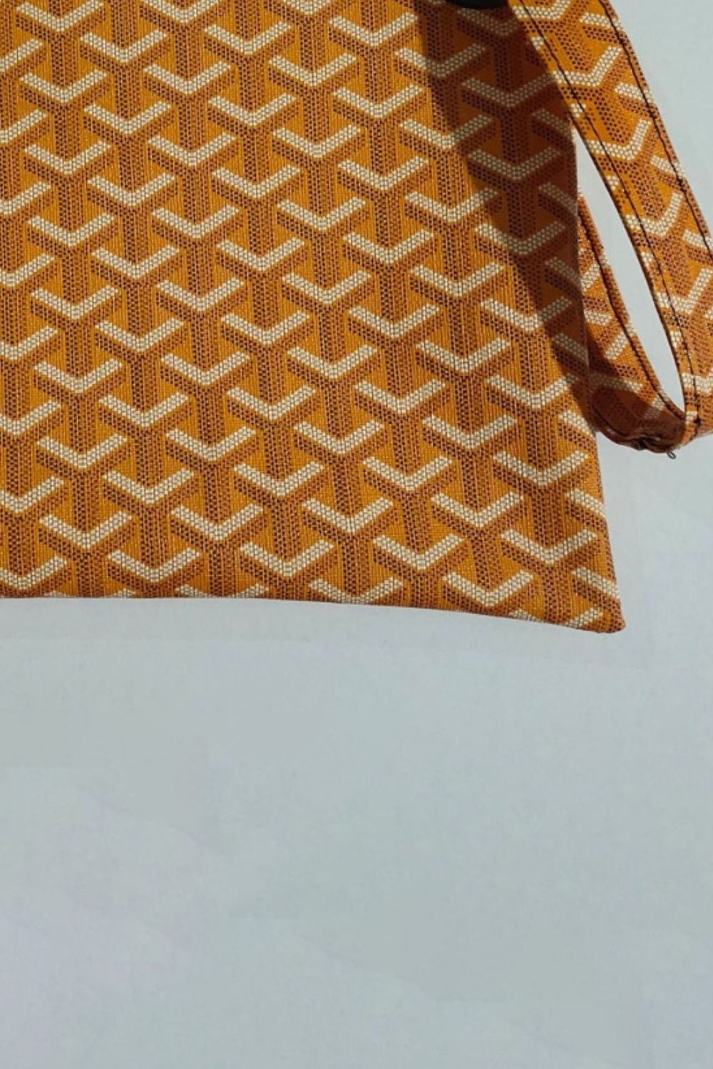 A medium rectangular orange-brown PU leather wristlet features a cream geometric pattern, clean stitched edges, and an attached wrist strap.