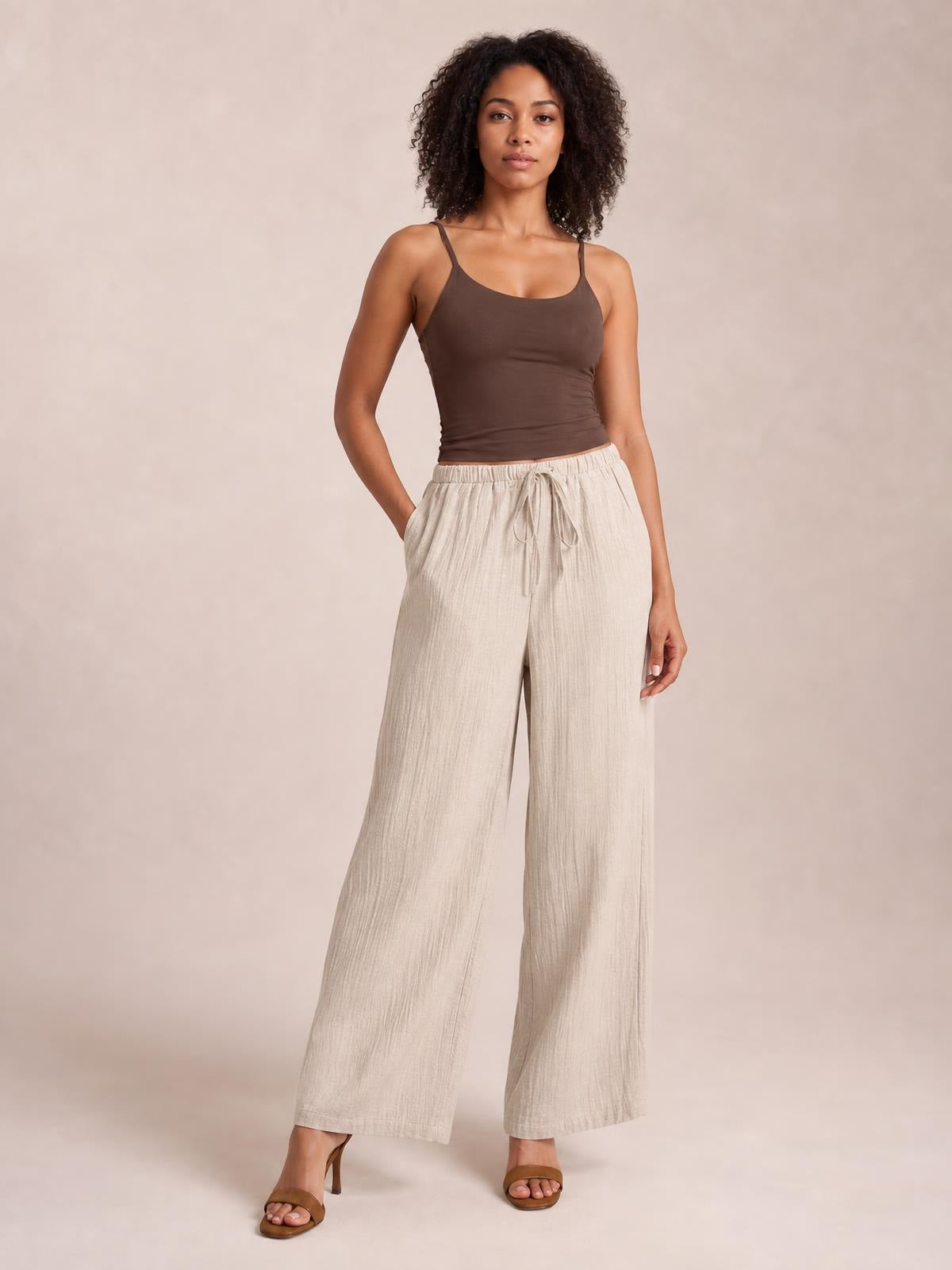 Model poses with one hand in a pocket, wearing light beige casual drawstring wide-leg pants with a relaxed silhouette and tied elastic waist.