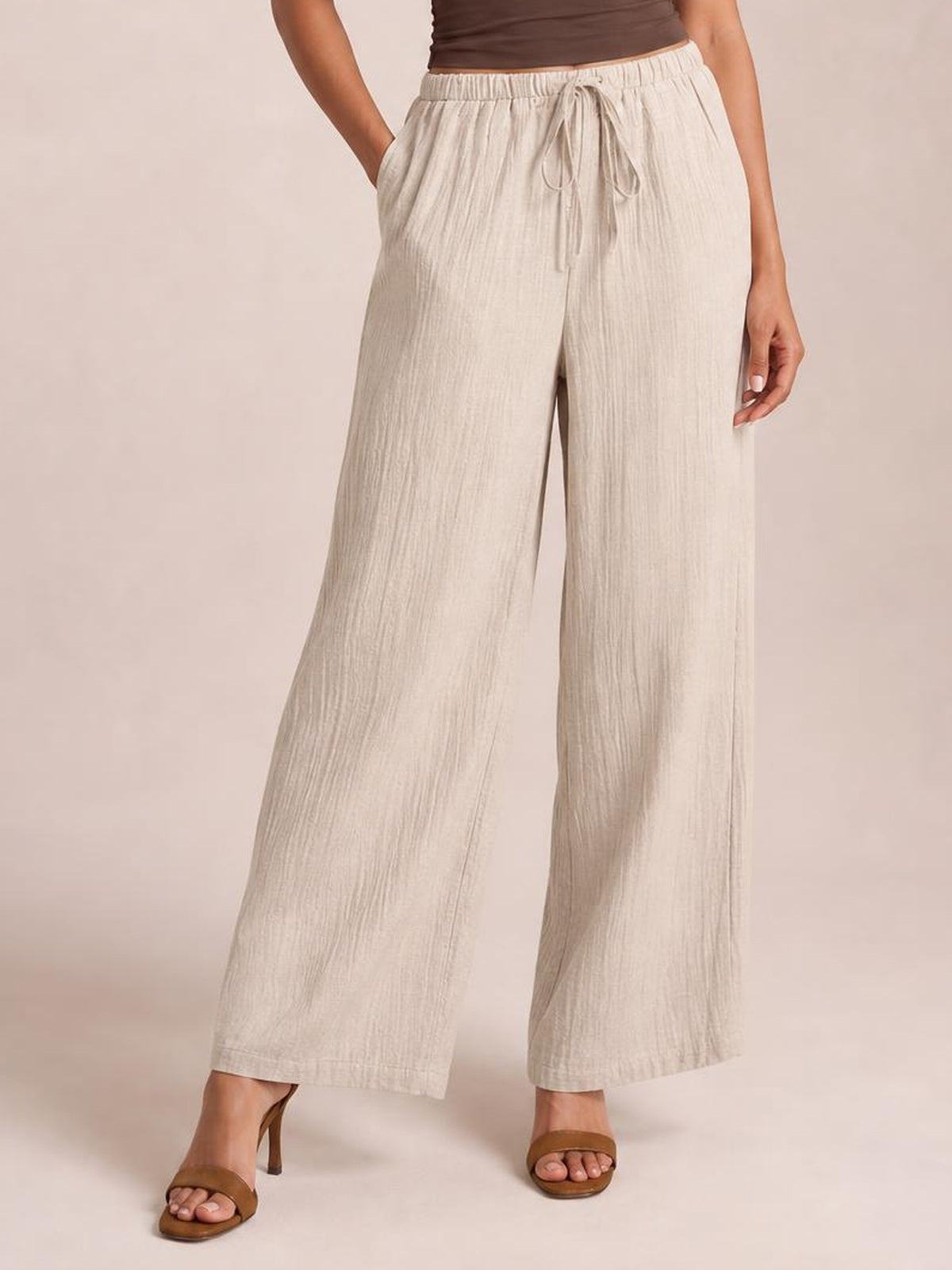 A model stands with one hand in a pocket, showcasing light beige casual drawstring wide-leg pants with an elastic waist and relaxed, flowing silhouette.