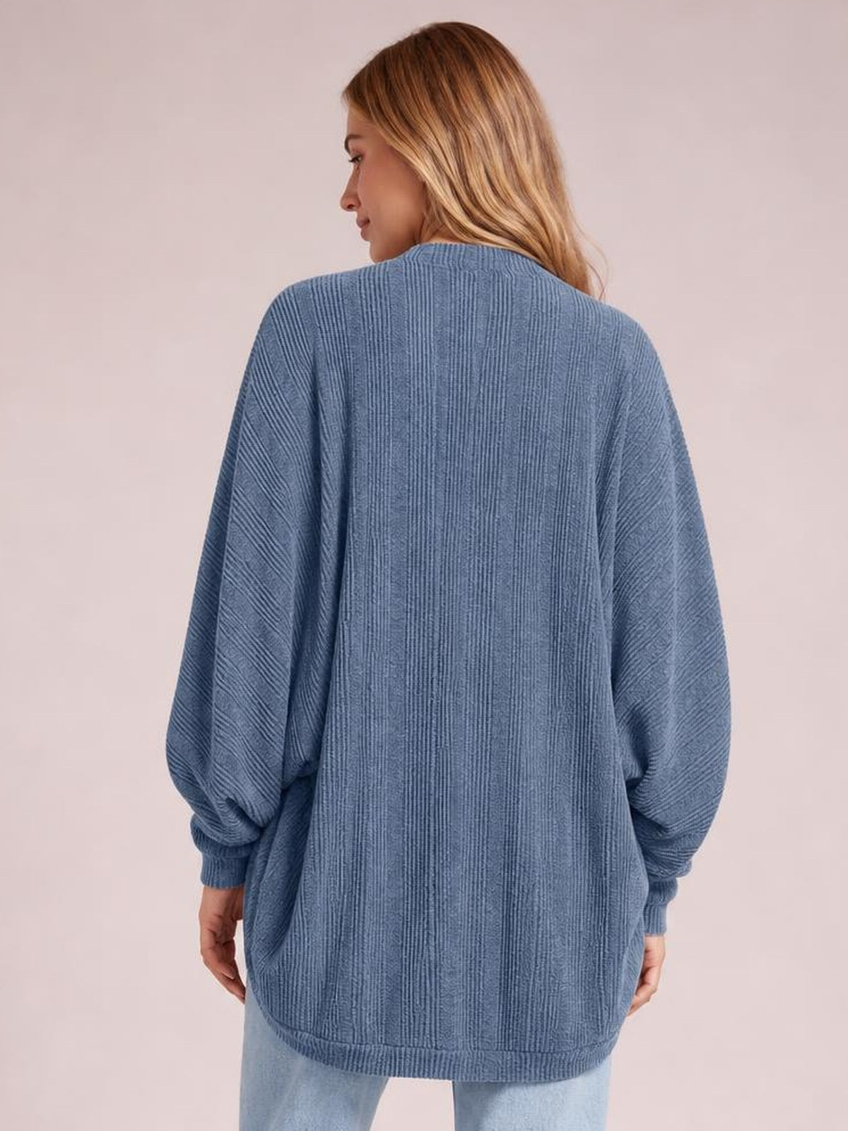 Model shown from the back wearing a blue knit open-front cardigan with a relaxed silhouette, long sleeves, ribbed cuffs, and a ribbed hem.