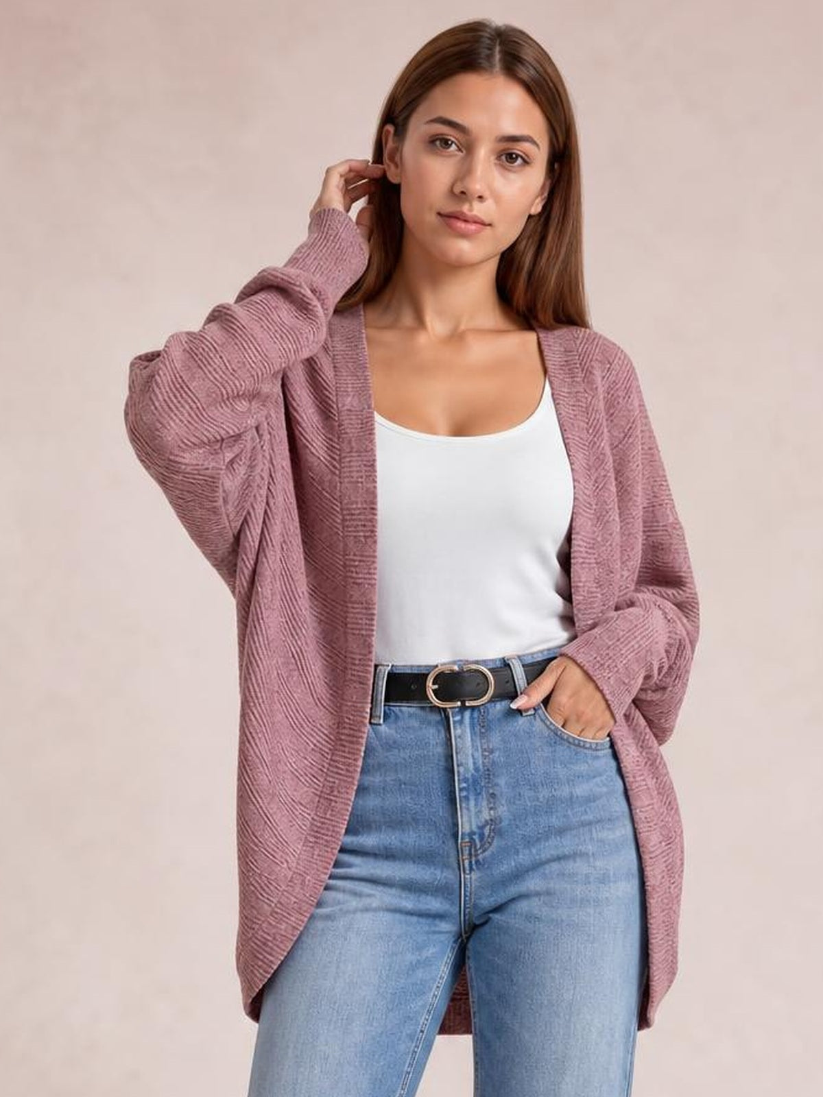 Model wears a mauve pink knit open-front cardigan with long sleeves and a relaxed longline silhouette over a white tank top and jeans.