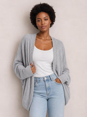 A model wears a light gray knit open-front cardigan with long sleeves and a relaxed draped silhouette over a white top and light-wash jeans.
