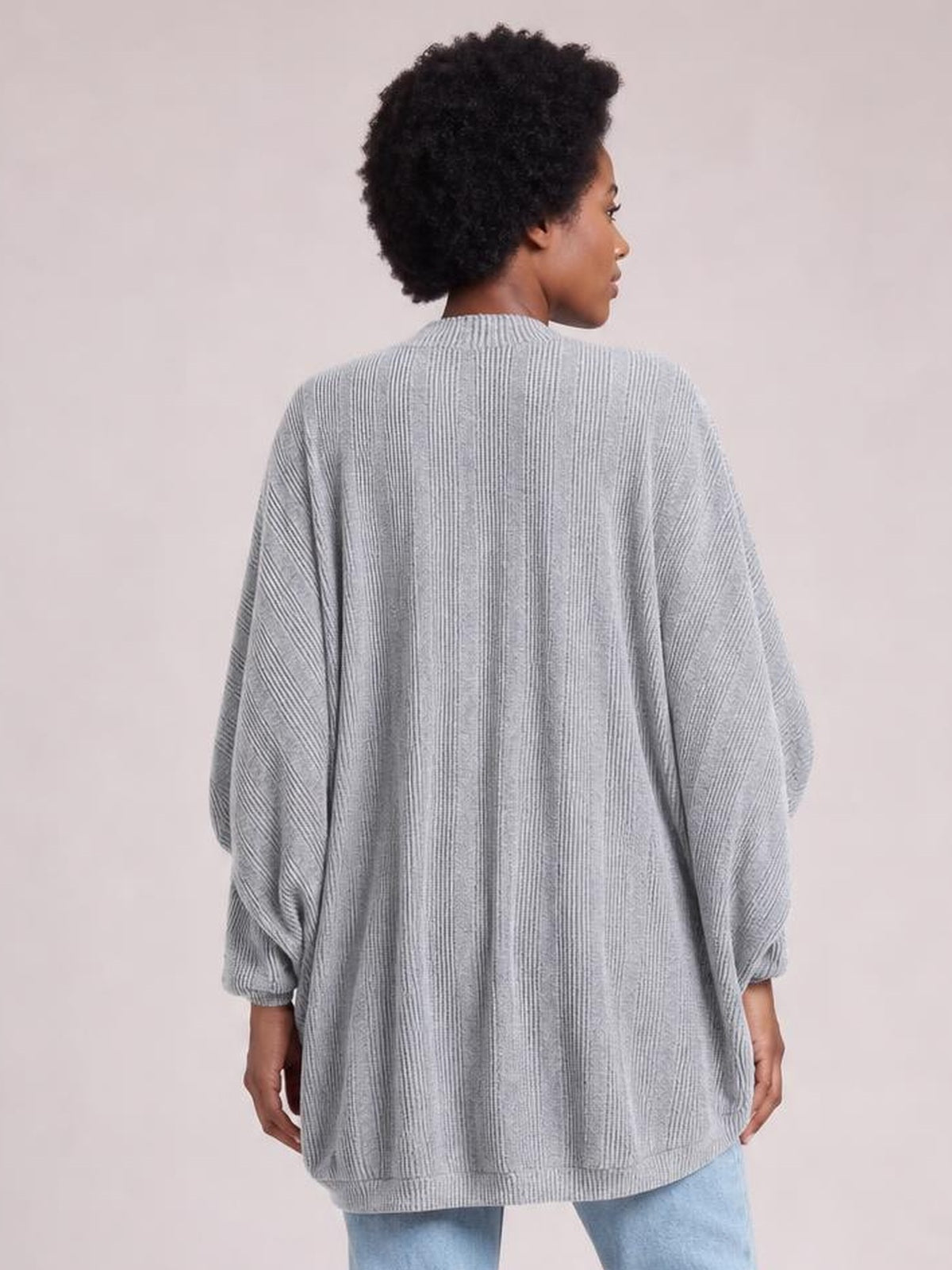 A model wears a light gray knit open-front cardigan with a relaxed oversized silhouette, vertical ribbed texture, long sleeves, and gathered cuffs.
