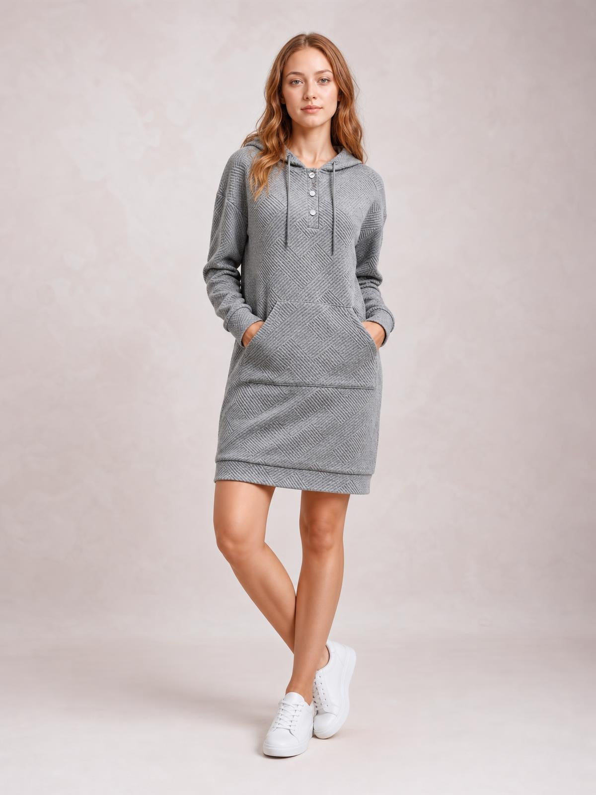 Model poses in a gray textured hooded sweatshirt dress with long sleeves, drawstring hood, button placket, front kangaroo pocket, and straight mini silhouette.