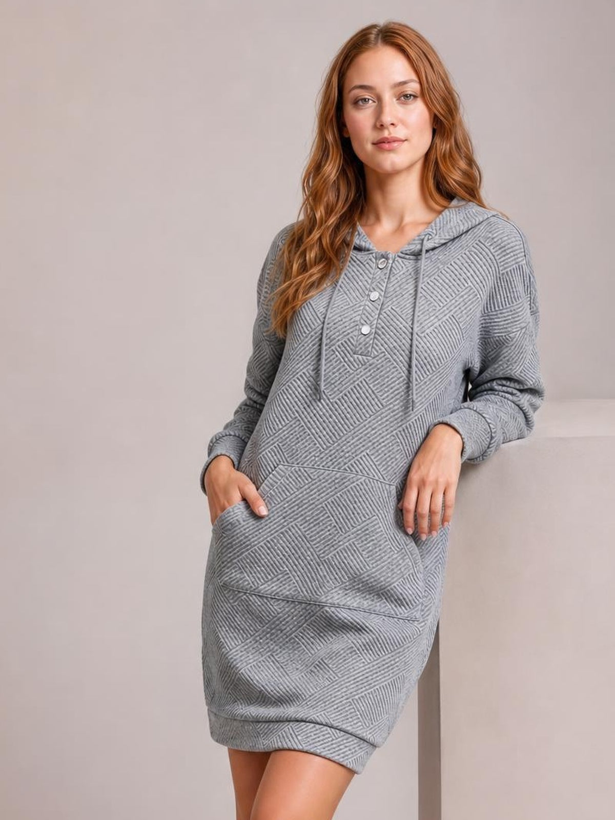 A model stands in a gray textured hooded sweatshirt dress with long sleeves, button placket, drawstrings, kangaroo pocket, and relaxed straight mini silhouette.