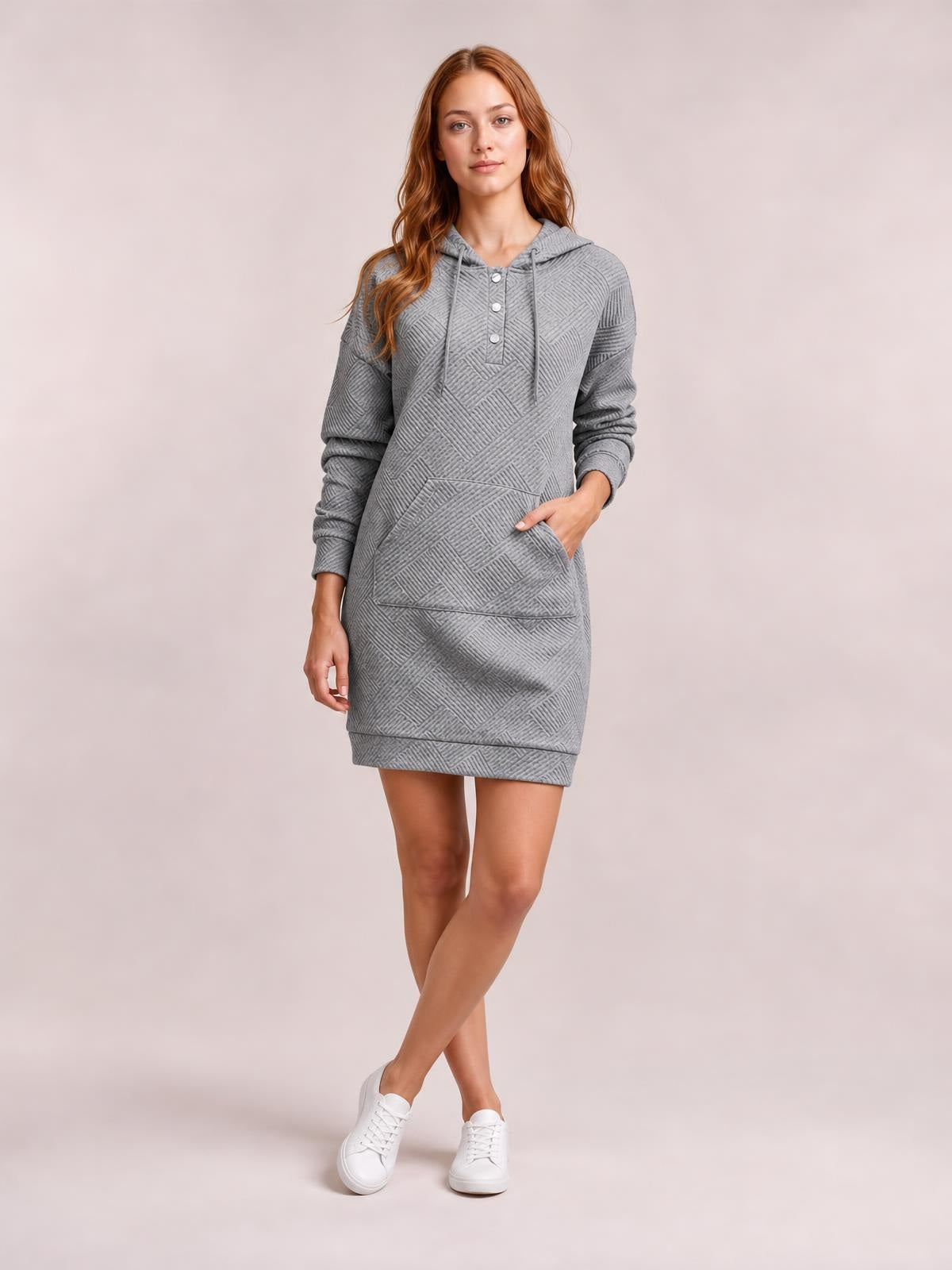 Model poses with crossed legs in a gray textured hooded sweatshirt dress featuring drawstrings, a button placket, long sleeves, kangaroo pocket, and straight above-knee silhouette.