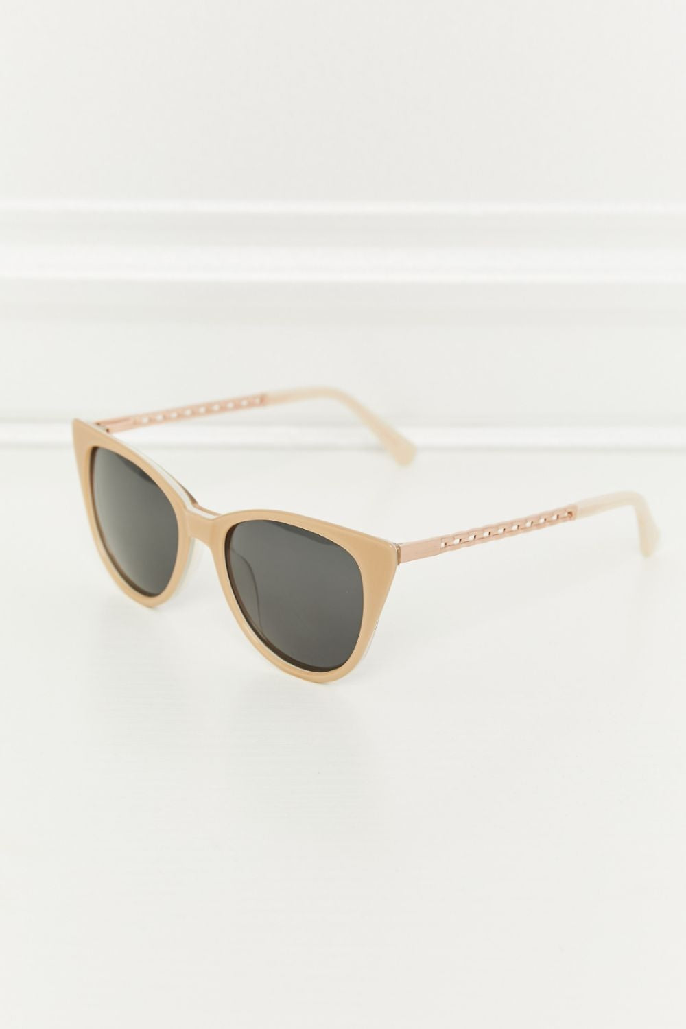 Tan acetate cat-eye sunglasses feature a softly upswept silhouette, dark lenses, and slender temples with refined metal and acetate detailing.