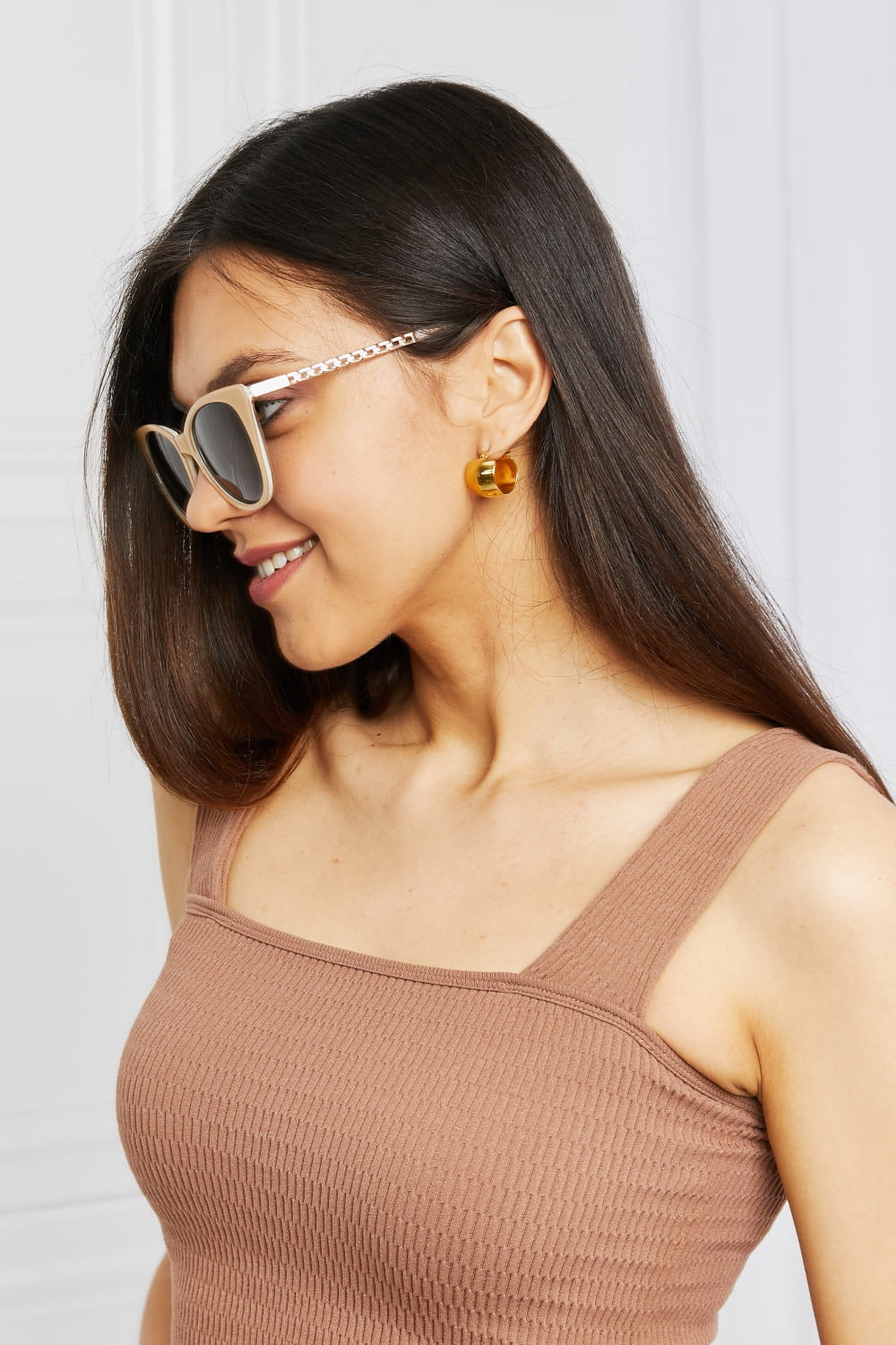 Model in profile wears cat-eye acetate sunglasses with a softly upswept beige frame, dark lenses, and metal-accented temples.