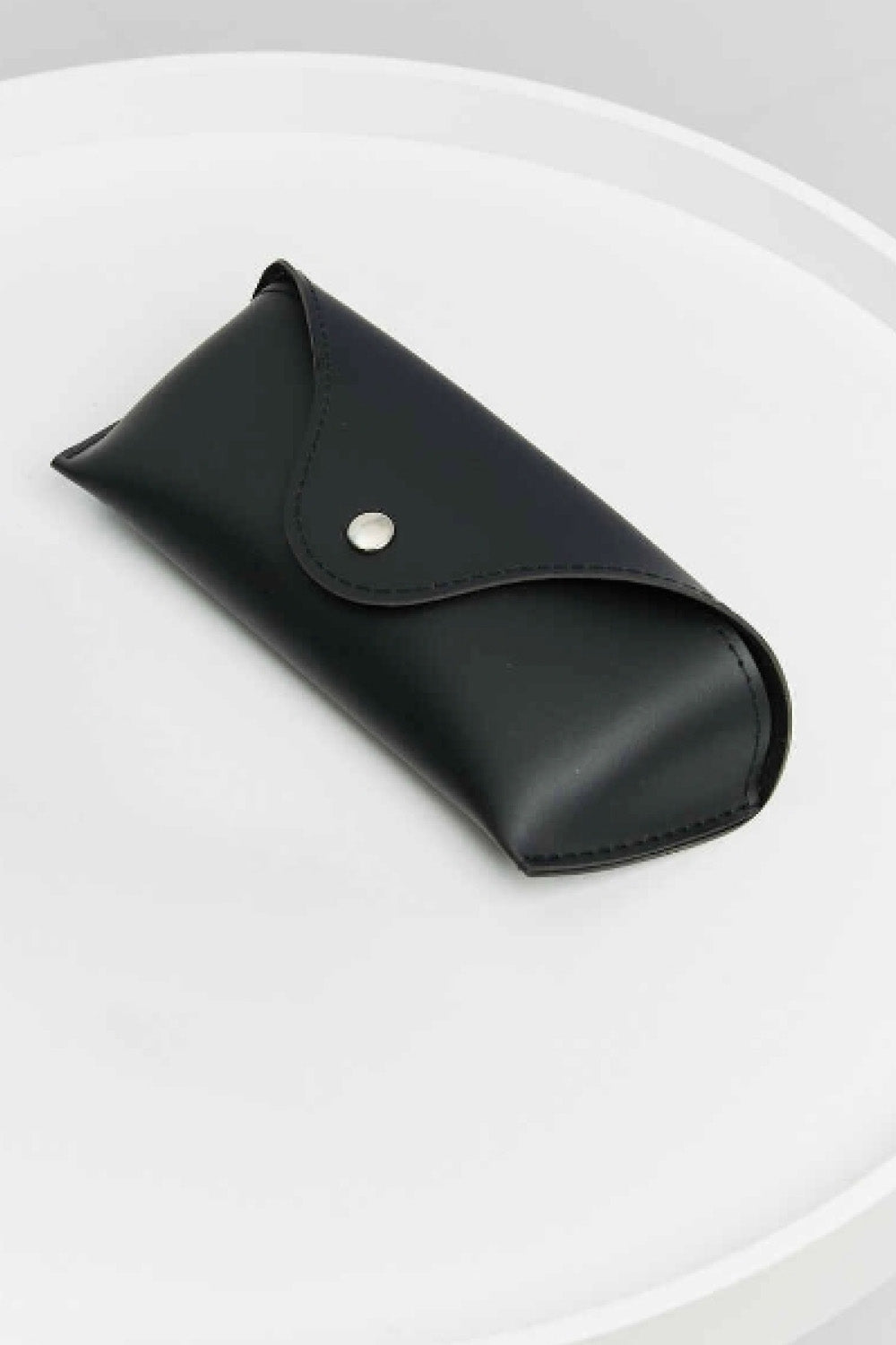A black sunglasses case with a structured rectangular silhouette, rounded edges, stitched seams, and a curved snap-flap closure with a metallic stud.