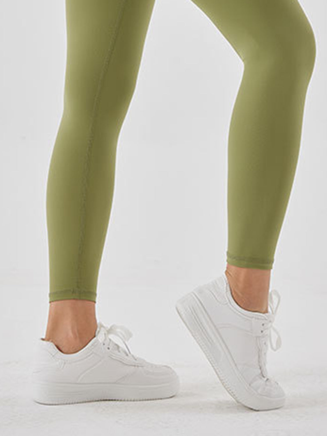 A model steps forward in olive green sports leggings with a close-fitting, full-length silhouette and smooth, stretchy construction.