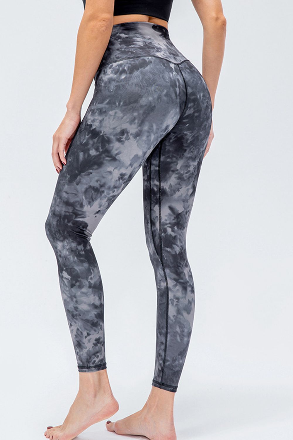 A model poses from the back in gray and black printed active leggings with a wide waistband, slim-fit silhouette, and visible leg seams.