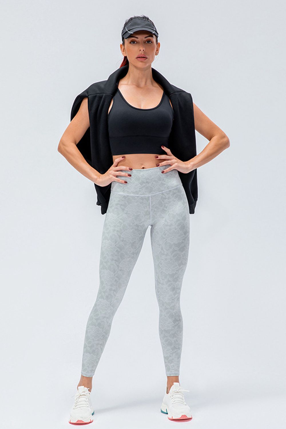 Model stands with hands on her hips wearing light gray patterned active leggings with a wide waistband and slim, full-length fit.