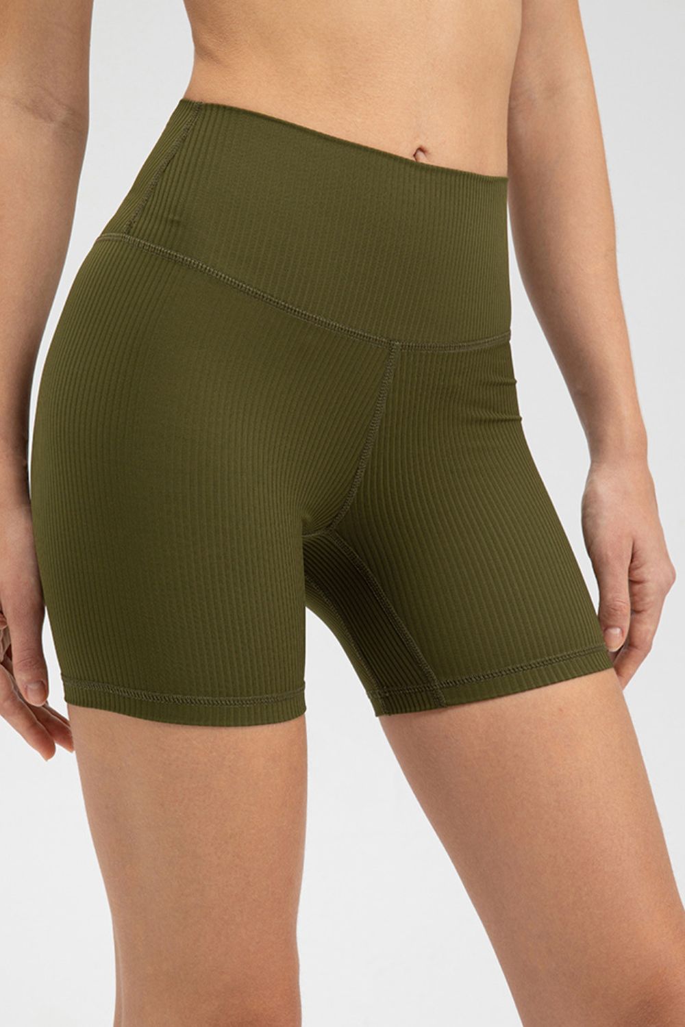 Model wearing olive green slim-fit sports shorts with a wide waistband, ribbed texture, mid-thigh silhouette, and visible seamed construction.