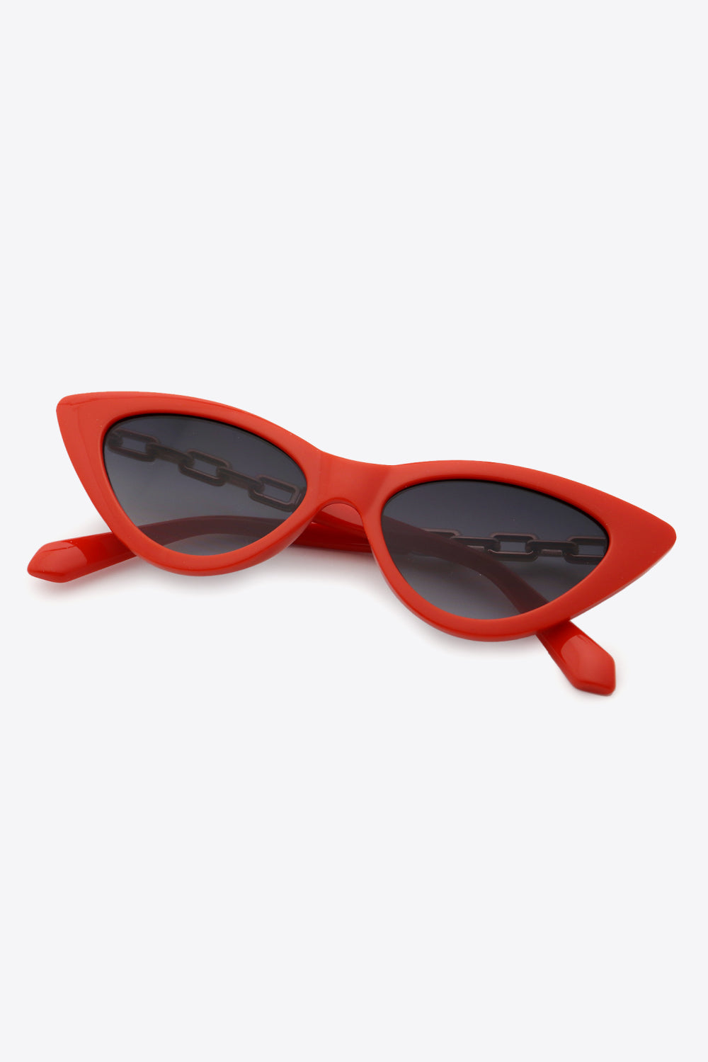 Red cat-eye sunglasses with a bold upswept silhouette, dark lenses, glossy red polycarbonate frames, and visible chain detailing along the temples.