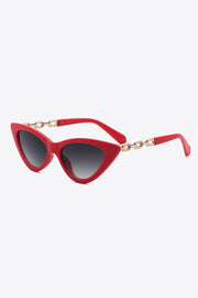 Red cat-eye sunglasses feature an upswept silhouette, dark lenses, and distinctive gold-tone chain detailing along the temples.