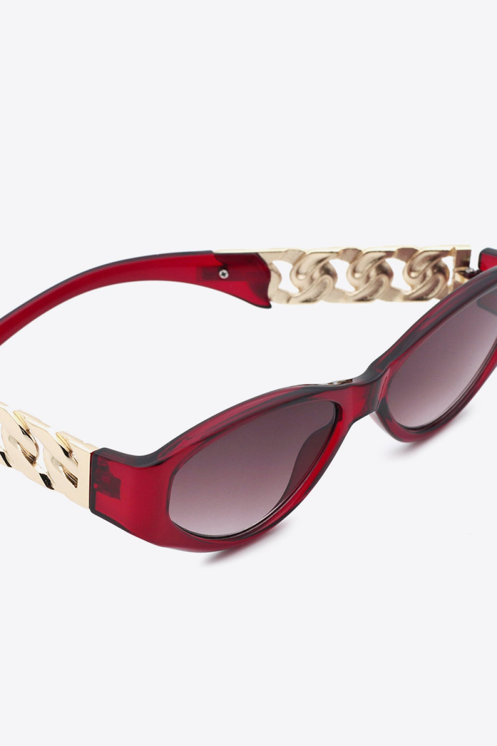 Red cat-eye sunglasses feature a bold upswept silhouette, dark gradient lenses, and polished gold chain-inspired temple details.