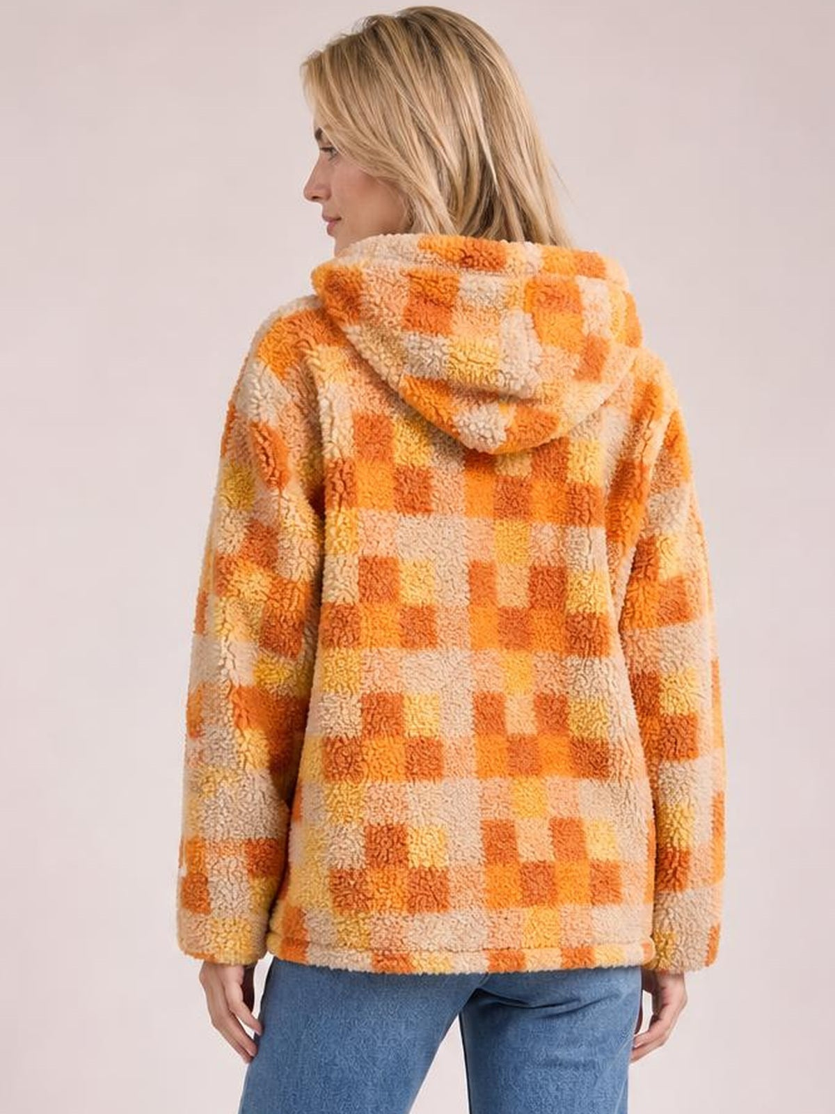 A model shows the back of an orange and cream checkered sherpa hooded jacket with long sleeves and a relaxed, softly structured silhouette.