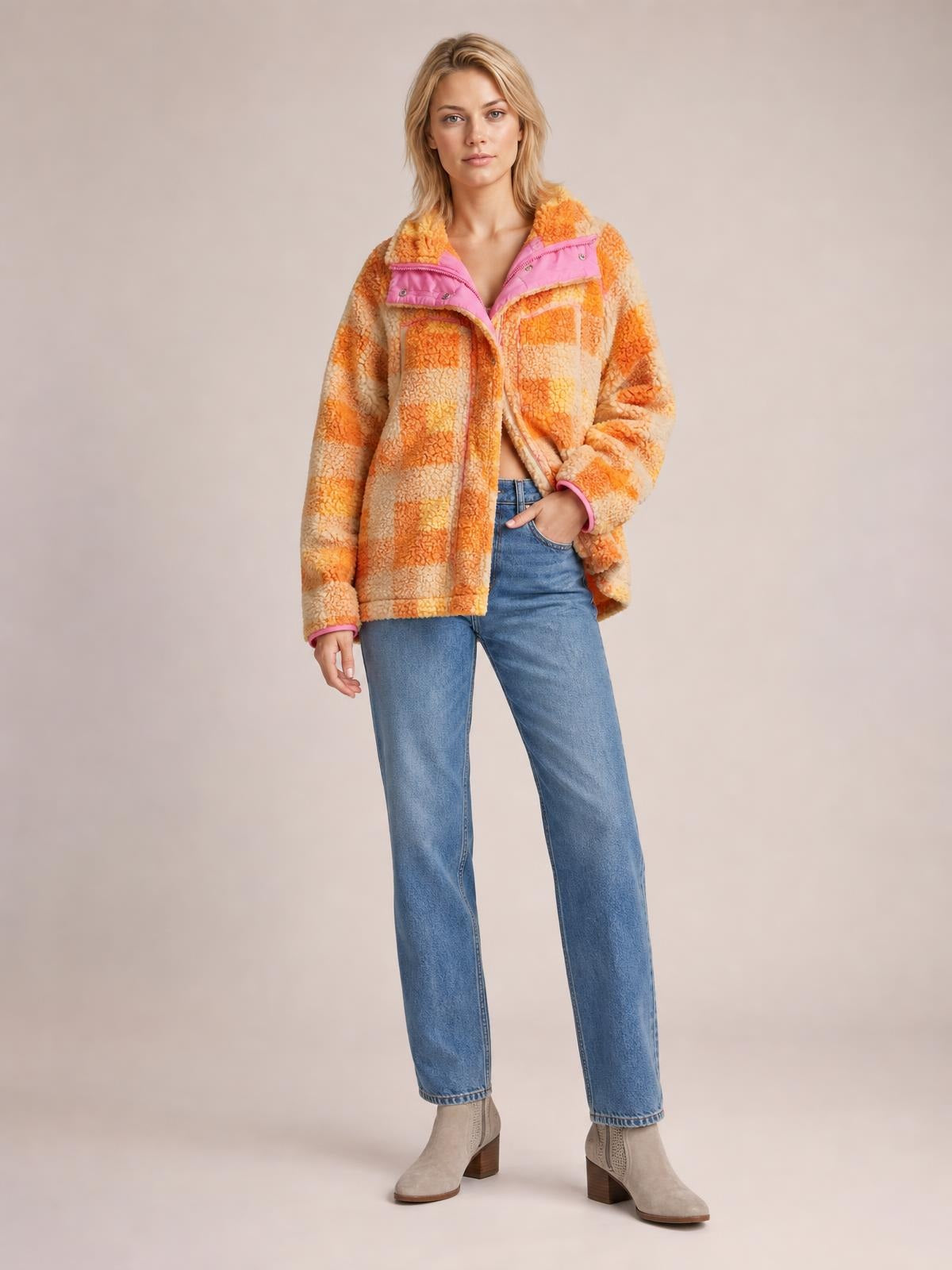 A model wears a relaxed checkered sherpa hooded jacket in orange and cream, featuring long sleeves, a zip front, pink trim, and a cozy textured silhouette.