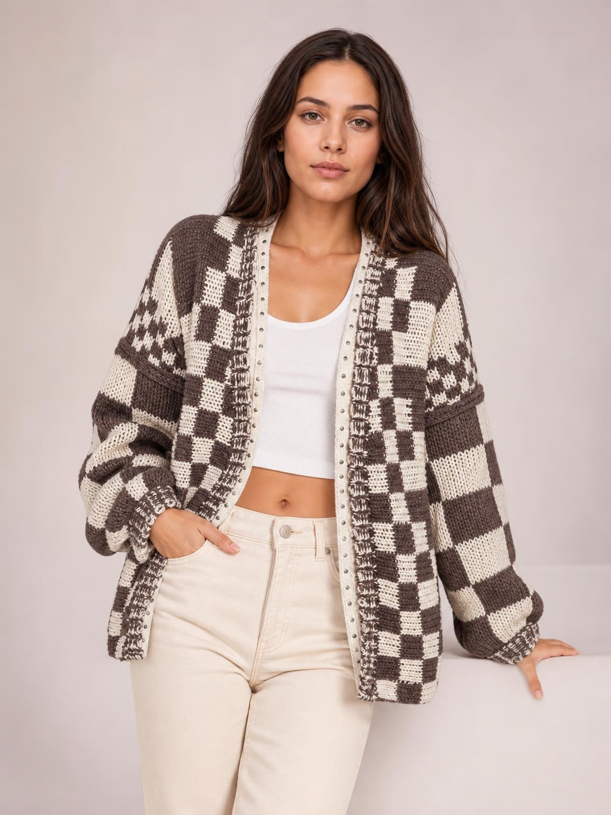 Model poses in a relaxed brown-and-cream checkered open-front cardigan with long sleeves, a loose silhouette, and ribbed cuffs over a white tank.