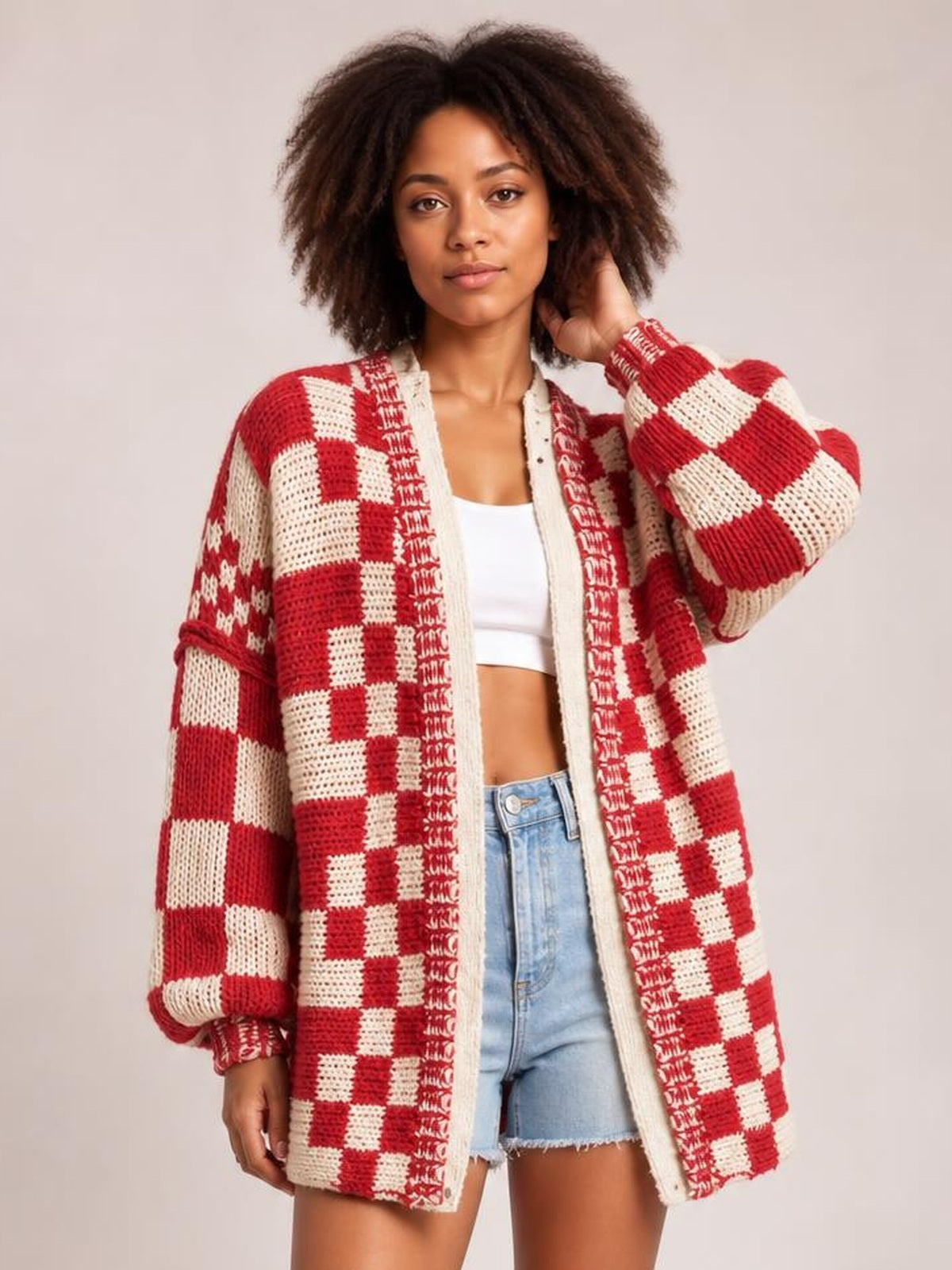 A model poses in a red and cream checkered open-front cardigan with long sleeves, a relaxed oversized silhouette, and textured knit construction.