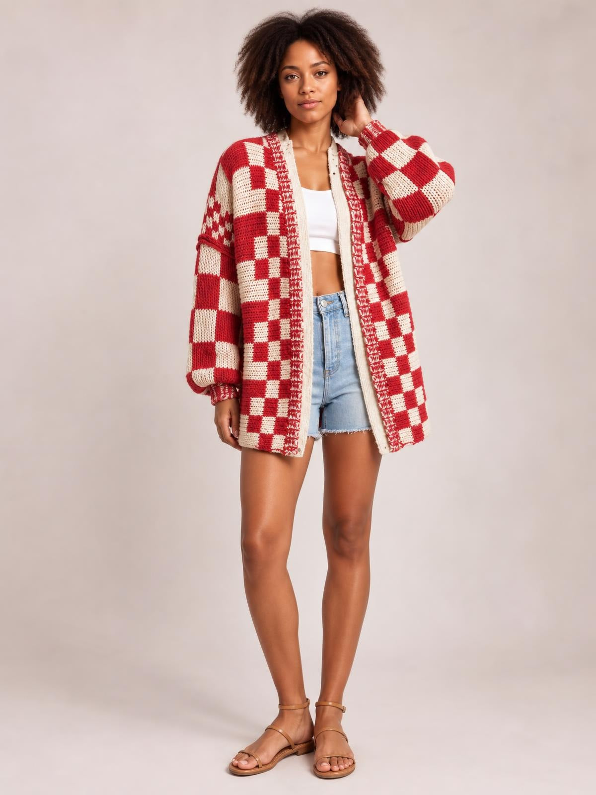 Model poses with one hand in her hair wearing a red and cream checkered open-front long-sleeve cardigan with a relaxed, long knit silhouette.