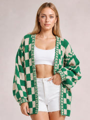 A model wears a green and cream checkered open-front long-sleeve cardigan with a relaxed silhouette, oversized sleeves, and one hand tucked into her shorts pocket.
