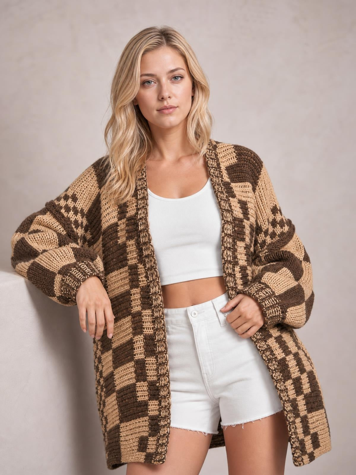 A model poses in a brown and beige checkered open-front cardigan with long sleeves, an oversized relaxed silhouette, and chunky textured knit construction.