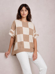 Model seated in a loose beige and cream checkered sweater with drop shoulders, short half sleeves, ribbed crew neckline and hem, and a relaxed silhouette.
