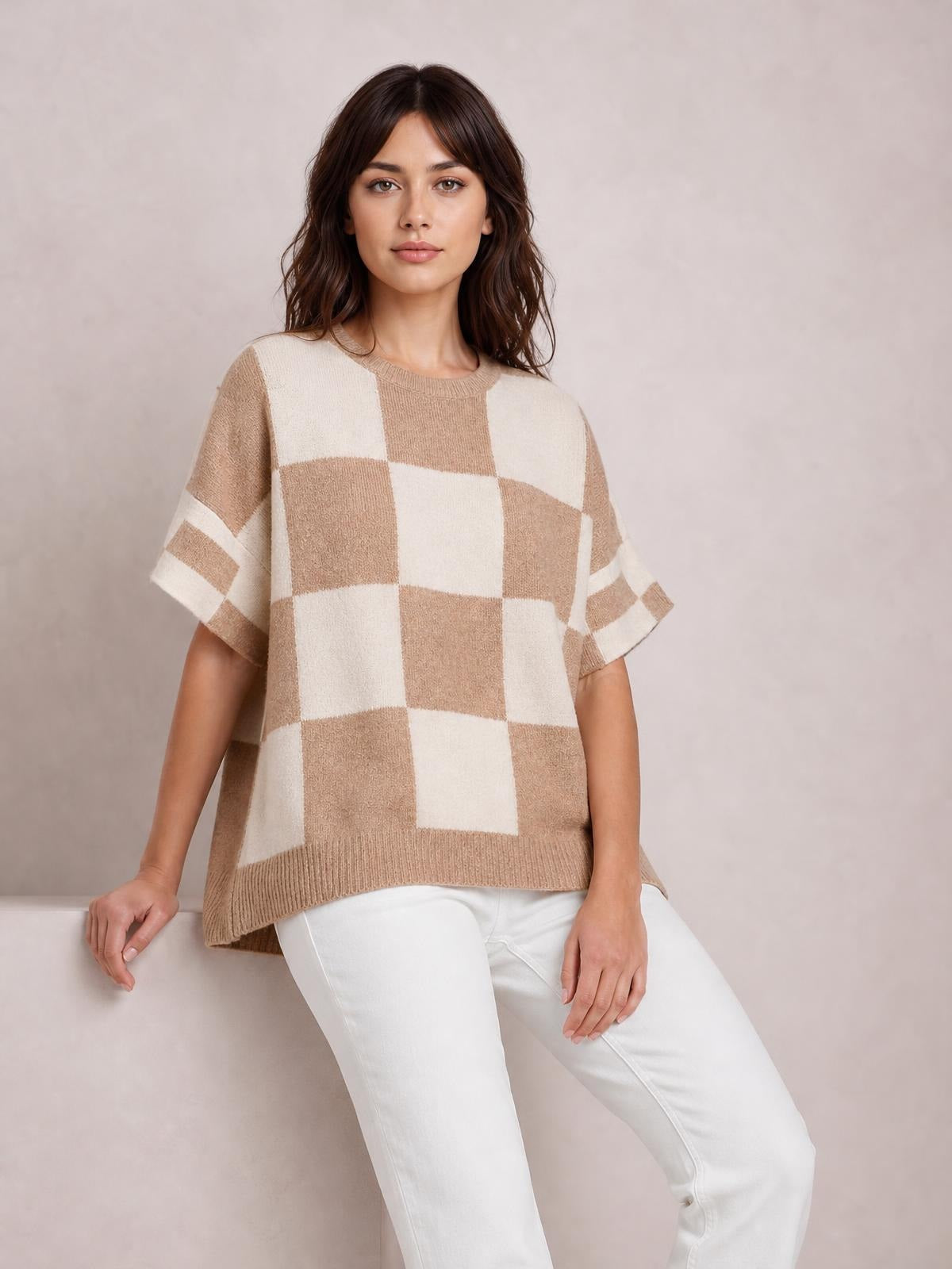 Model seated in a loose beige and cream checkered sweater with drop shoulders, short half sleeves, ribbed crew neckline and hem, and a relaxed silhouette.