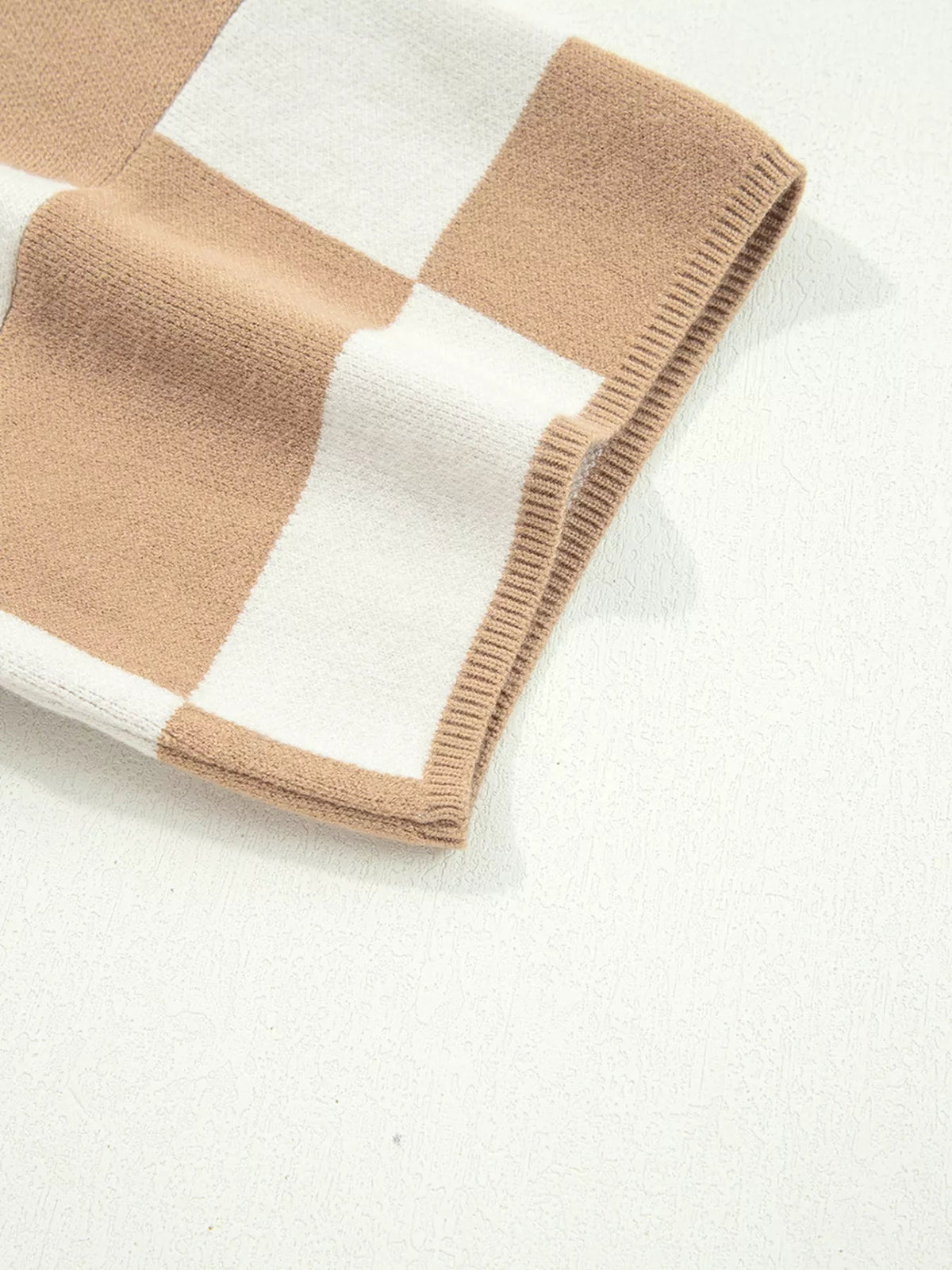 Close-up of a beige and white checkered knit sweater showing its soft texture, loose construction, and ribbed sleeve and hem edges.