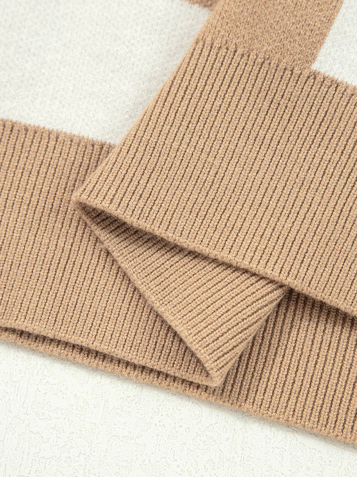 Close-up of a camel-brown knit sweater showing its ribbed texture, overlapping fabric panels, and neatly finished sleeve cuff construction.