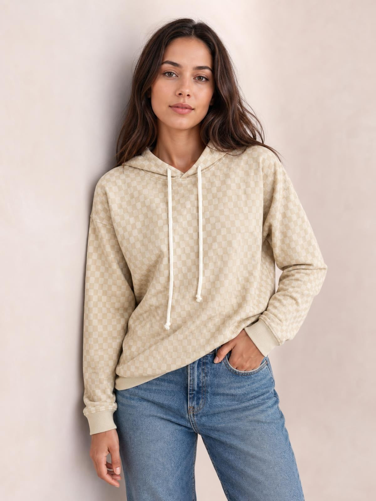 Model wears a relaxed cream checkered hoodie with a drawstring hood, long sleeves, ribbed cuffs and hem, posing with one hand in her jeans pocket.