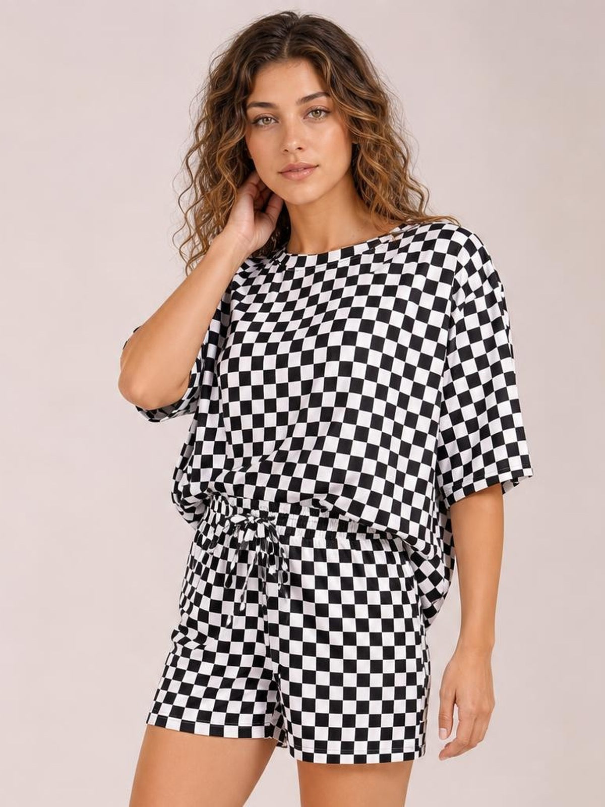 Model poses in a black-and-white checkered top and shorts set featuring a round neck, relaxed silhouette, and drawstring waist.