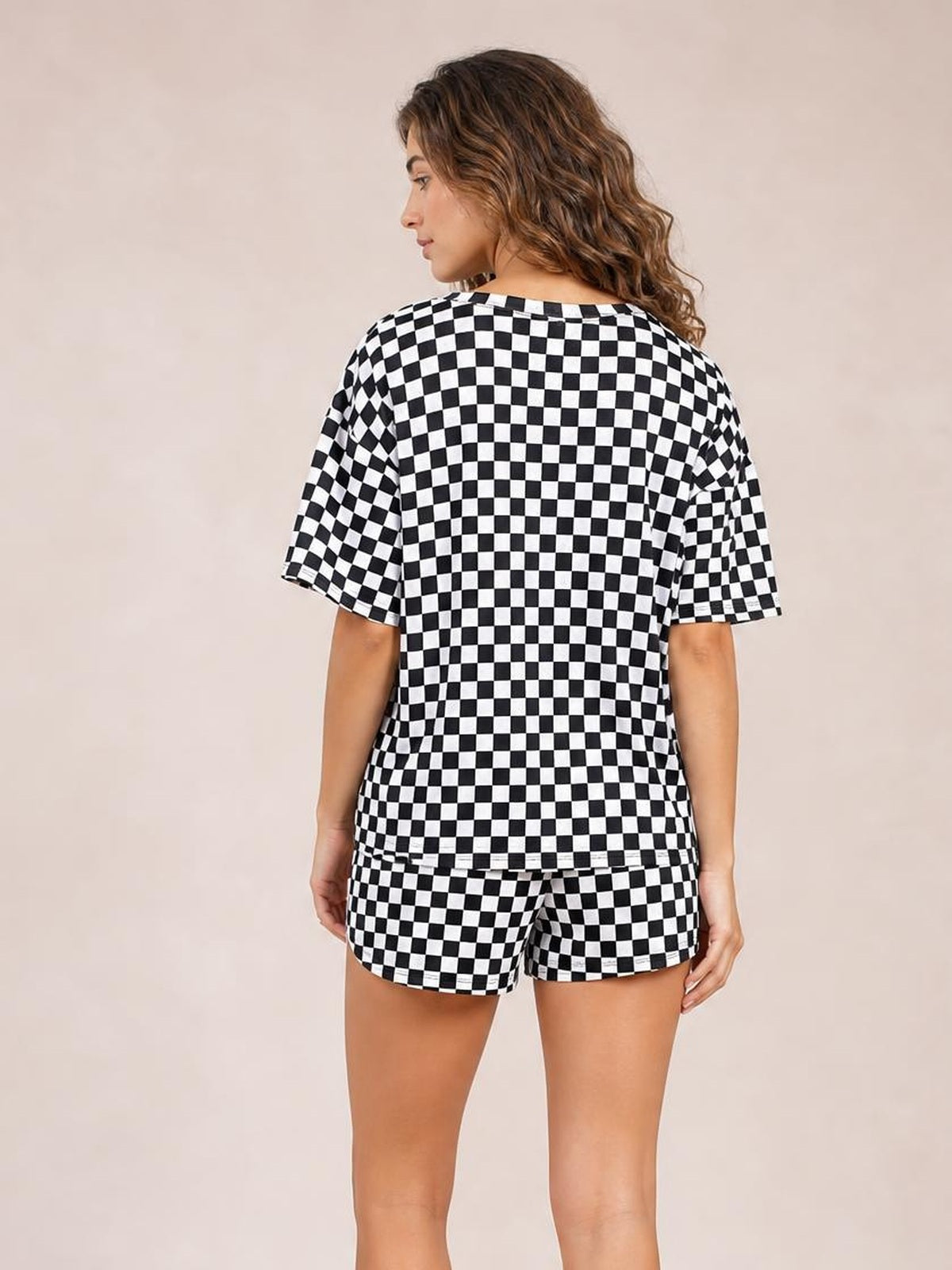 Model shown from the back wearing a black-and-white checkered round neck top and relaxed drawstring shorts set, with short sleeves and an easy silhouette.