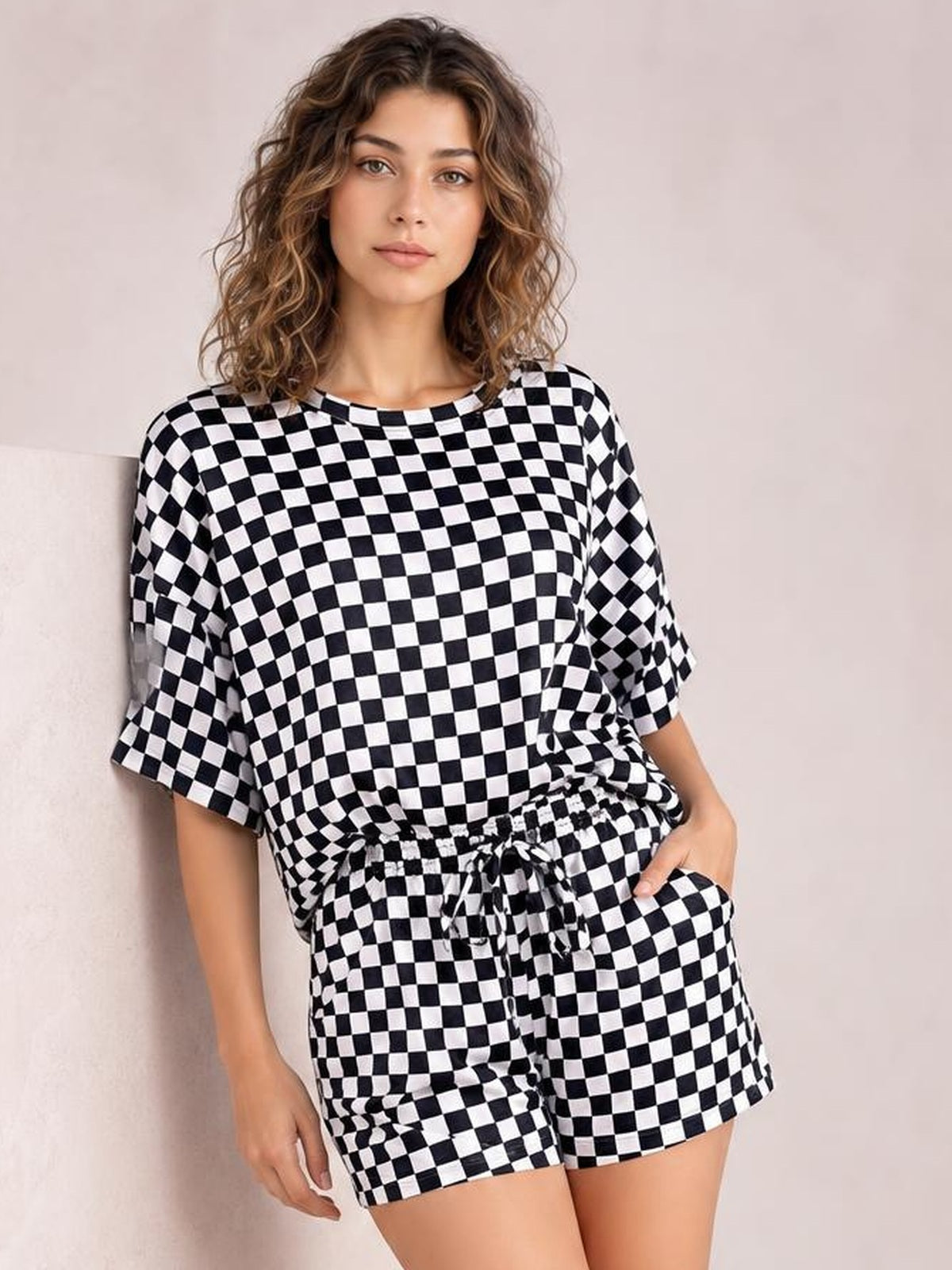 Model wearing a black-and-white checkered round neck top and matching drawstring shorts set, with a relaxed oversized silhouette and one hand in a pocket.
