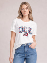 Model wearing a white checkered USA graphic round neck tee with short sleeves and a relaxed silhouette, standing with one hand in her jeans pocket.