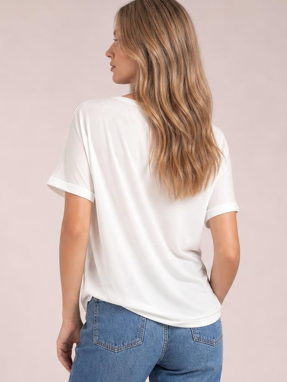 Model shown from the back in a white round neck tee with rolled short sleeves and a relaxed, slightly loose silhouette, turning to one side.