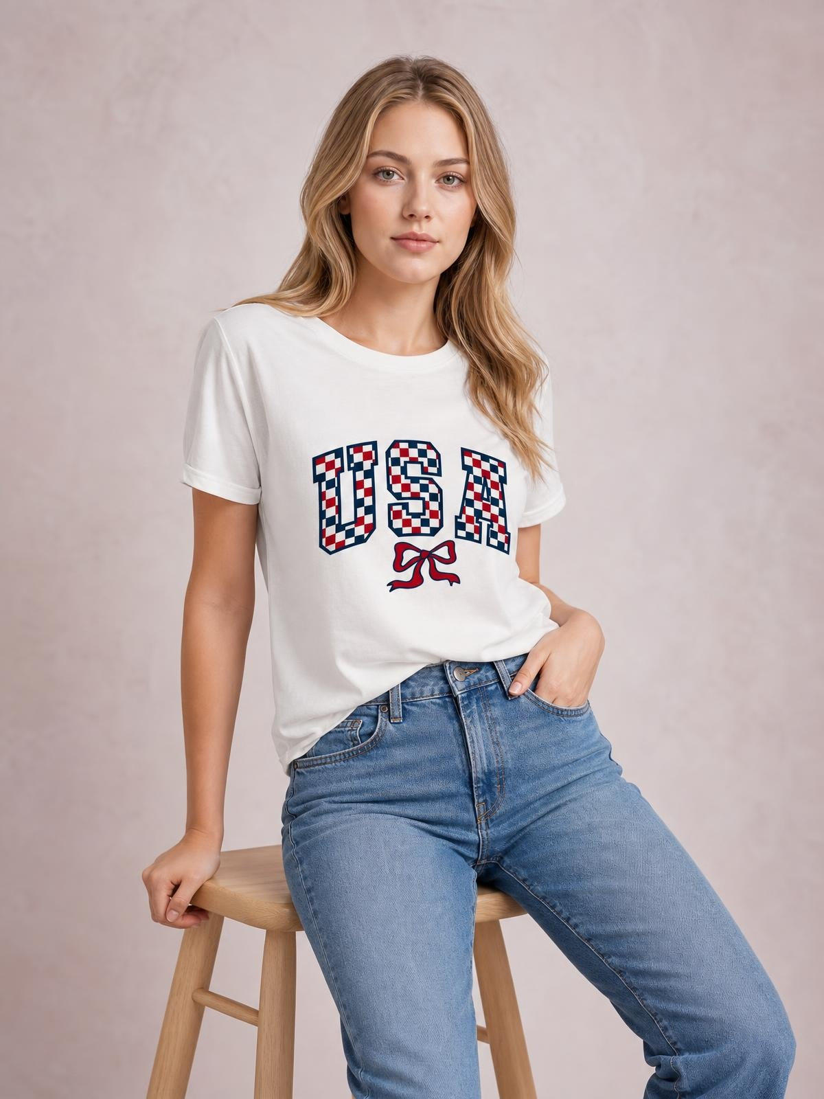 Model seated in a white checkered USA graphic round neck tee with short sleeves and a relaxed silhouette, paired with blue jeans.