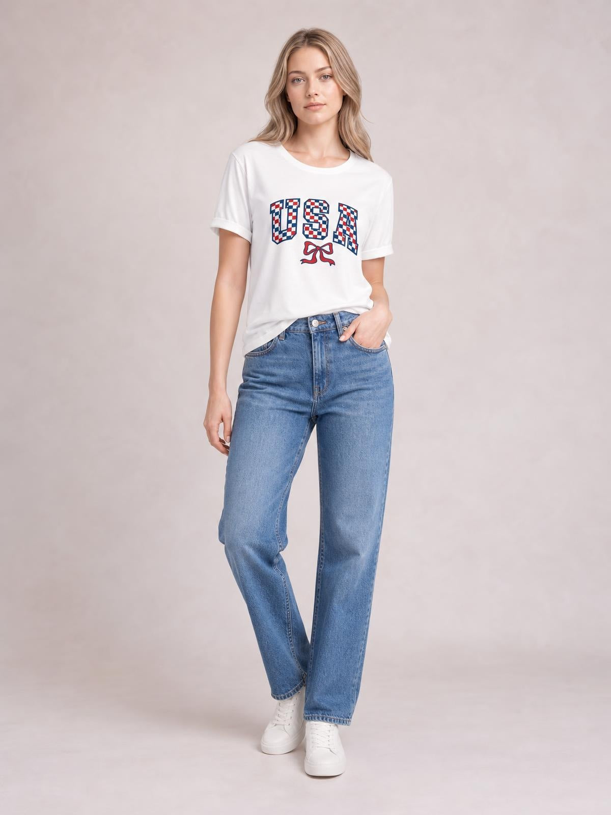 Model wearing a white checkered USA graphic round neck tee with short sleeves and a relaxed silhouette, posed with one hand in her jeans pocket.