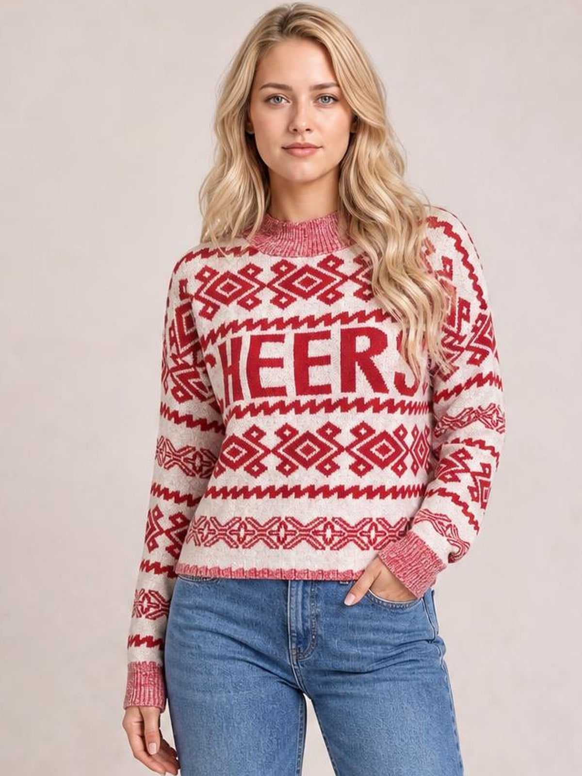 Model poses with one hand in her jeans pocket wearing a cream-and-red CHEERS Christmas sweater with a round neck, long sleeves, ribbed trim, and a relaxed silhouette.